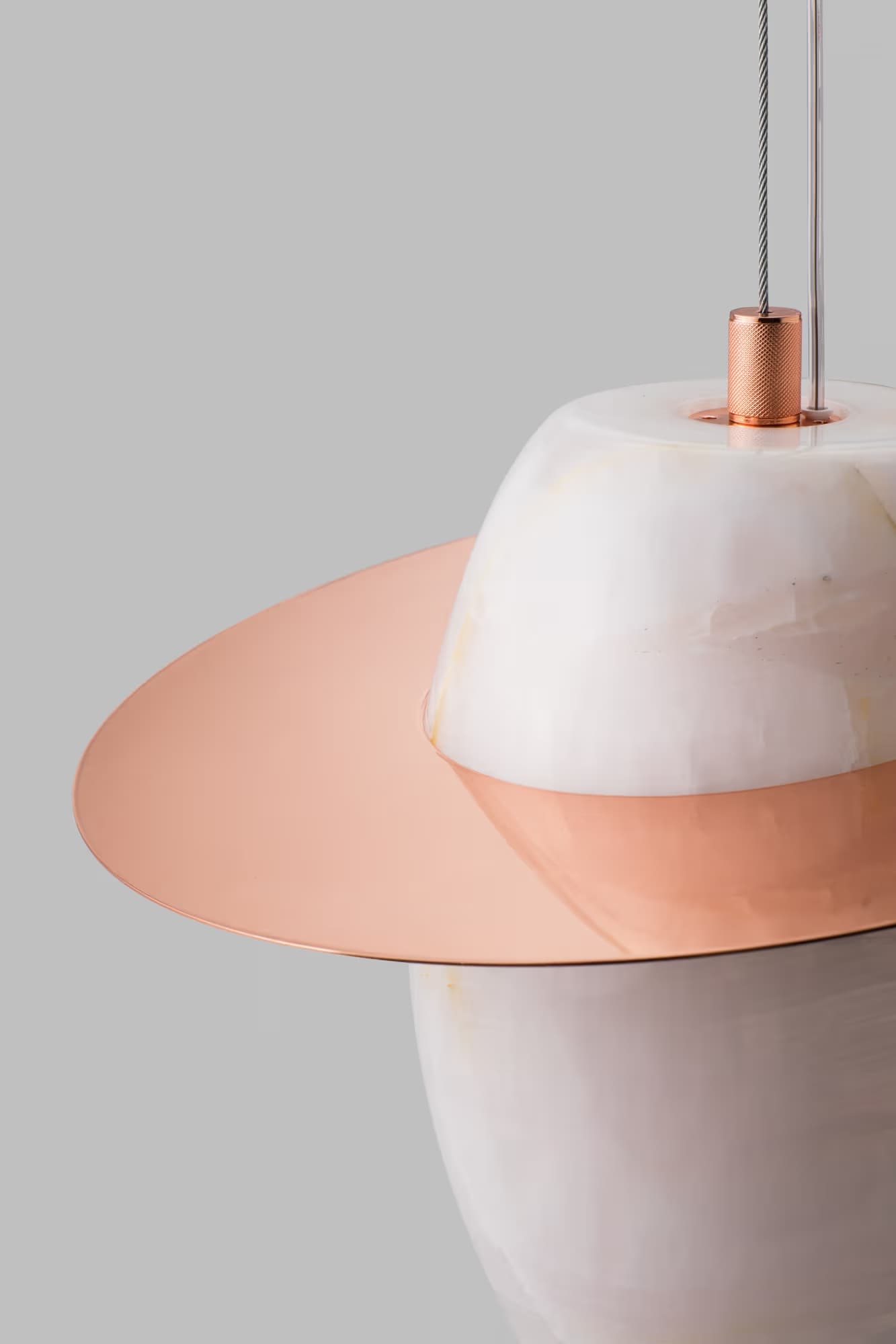Close-up of a modern pendant light with a white marble body and a flat copper disc, luxury contemporary lighting design